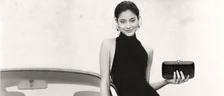 Woman in a black dress holding a clutch next to a car